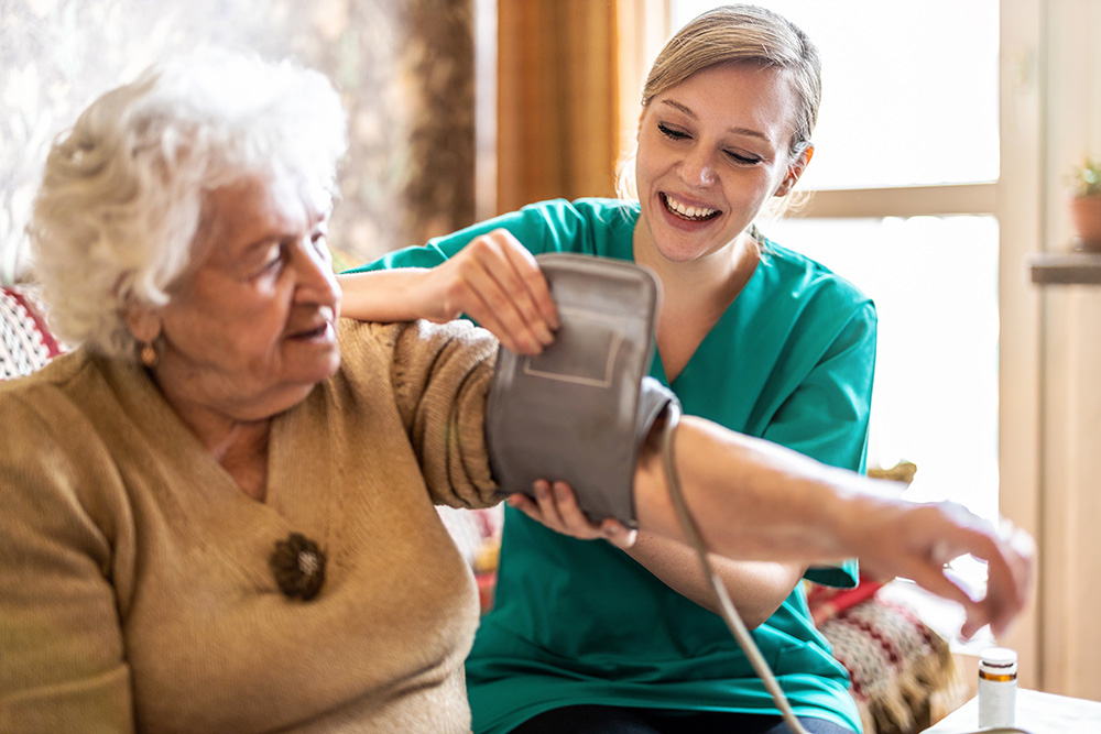 GettyImages-1307432717 Health aide measuring senior woman's blood pressure at home