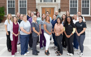 Smiling group of staff standing outdoors in front of a brick building.